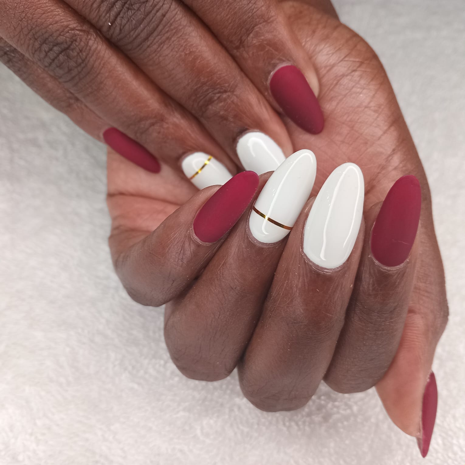Matte burgundy and glossy white almond nails with gold stripe detail by Laira Touch